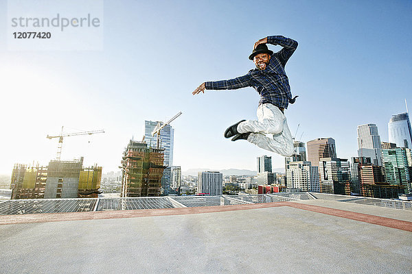 Schwarzer Mann tanzt und springt auf dem Dach einer Stadt