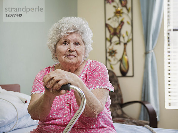 Ernste kaukasische Frau sitzt auf einem Bett und stützt sich auf einen Stock