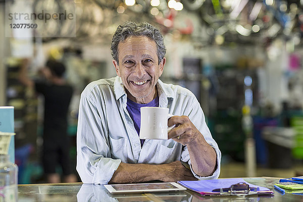 Porträt eines lächelnden kaukasischen Mannes  der in einem Fahrradgeschäft Kaffee trinkt