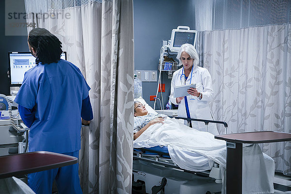 Arzt mit digitalem Tablet im Gespräch mit einem Patienten im Krankenhausbett