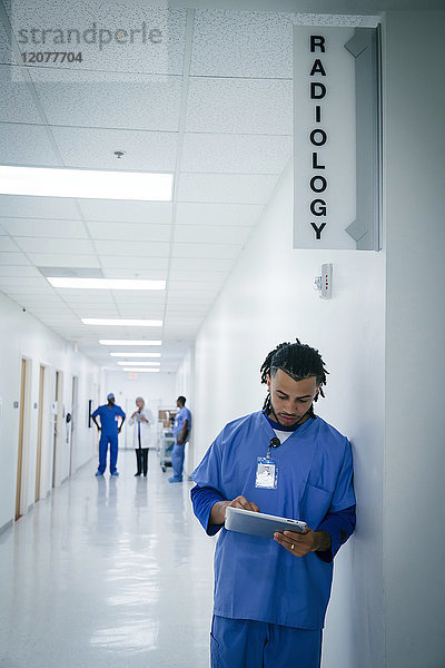 Krankenschwester lehnt an einer Wand im Krankenhaus und benutzt ein digitales Tablet