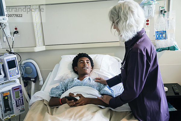 Arzt tröstet Jungen im Krankenhausbett mit Handy in der Hand