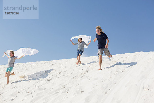 Kaukasischer Junge und Mädchen laufen auf einer Sanddüne