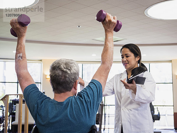 Physiotherapeutin hilft Mann beim Heben von Gewichten