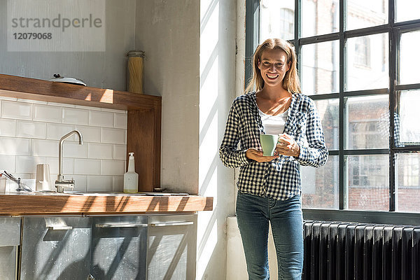 Junge Unternehmerin in der Firmenküche stehend  Kaffee trinkend