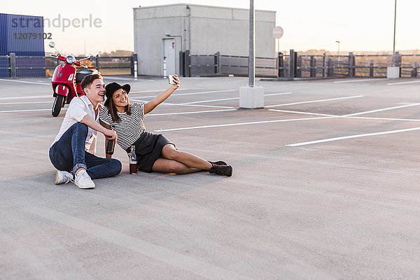Glückliches junges Paar mit Motorroller auf Parkebene mit einem Selfie