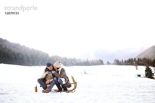 Seniorenpaar sitzend nebeneinander auf Schlitten in verschneiter Landschaft