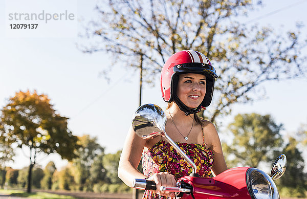 Porträt der lächelnden jungen Frau auf dem Motorroller