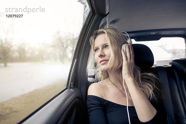 Porträt einer jungen Frau  die im Auto sitzt und Musik mit Kopfhörern hört.