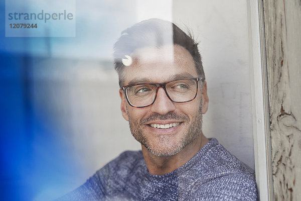 Porträt des lächelnden Mannes hinter Glasscheibe mit Brille
