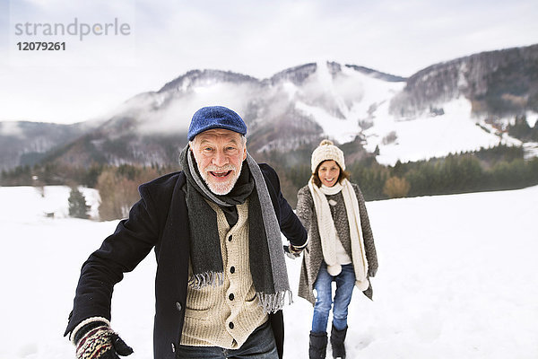 Porträt eines älteren Mannes  der Hand in Hand mit seiner Frau in schneebedeckter Landschaft geht