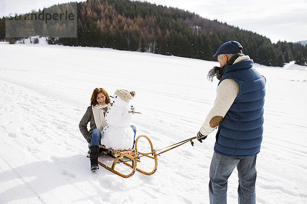 Seniorenpaar mit Schneemann auf Schlitten in Winterlandschaft