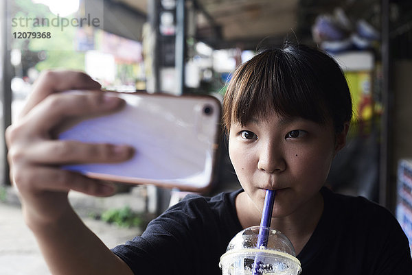 Porträt einer Frau  die Smoothie trinkt  während sie Selfie mit dem Smartphone nimmt.