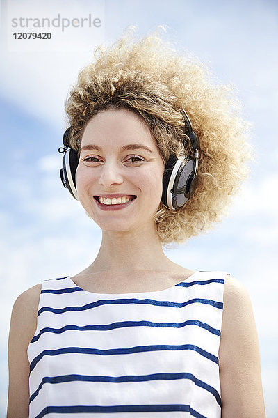 Porträt einer lachenden jungen Frau beim Musikhören mit Kopfhörern