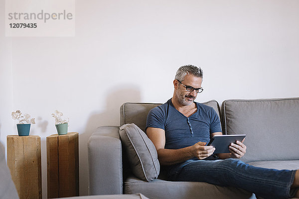 Erwachsener Mann  der zu Hause auf der Couch sitzt und Tabletten benutzt.