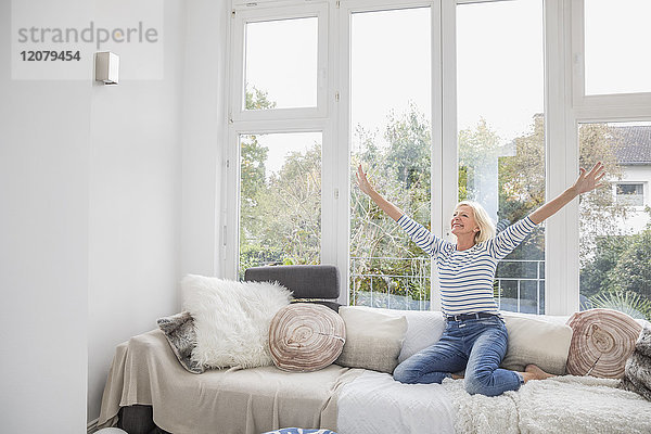 Fröhliche Seniorin auf der Couch im Wohnzimmer