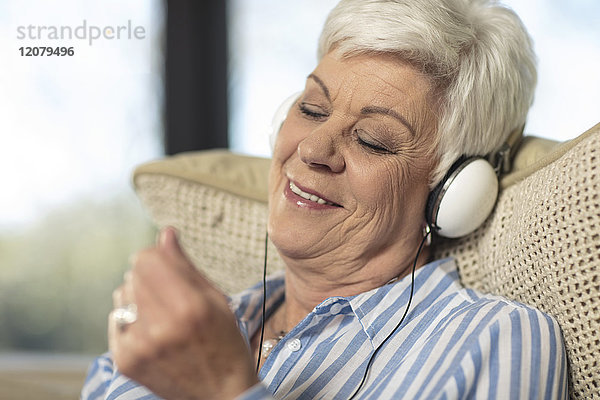 Lächelnde Seniorin mit Kopfhörer  die zu Hause Musik hört.