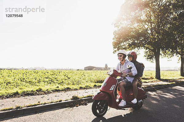 Fröhliches junges Paar beim Motorrollerfahren auf der Landstraße