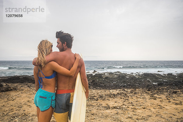 Junges Paar mit Surfbrett am Strand stehend
