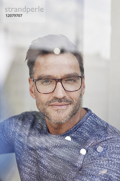Porträt des lächelnden Mannes hinter Glasscheibe mit Brille