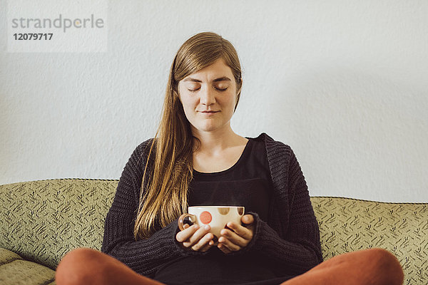 Frau mit geschlossenen Augen sitzend auf der Couch mit Teetasse