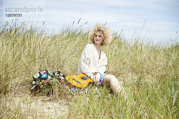 Porträt einer jungen Frau mit Gitarre  die sich in Stranddünen entspannt.