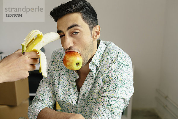 Porträt eines lässigen Geschäftsmannes mit Banane im Tempel und Apfel im Mund