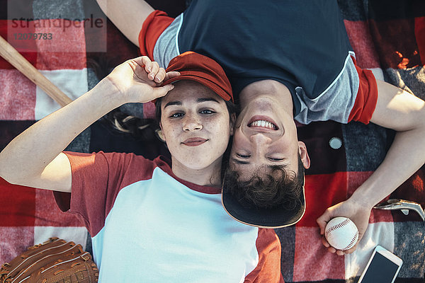 Porträt eines lächelnden jungen Paares mit Baseballausrüstung auf einer Decke liegend