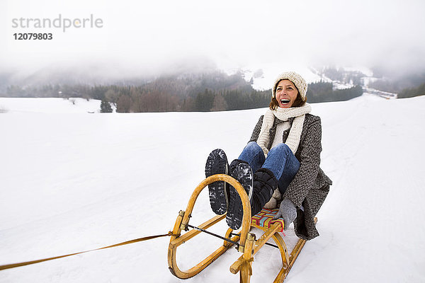 Lachende Seniorenfrau auf Schlitten in verschneiter Landschaft