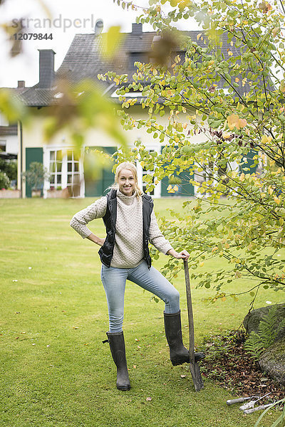 Porträt der lächelnden jungen Frau mit Spaten im Garten