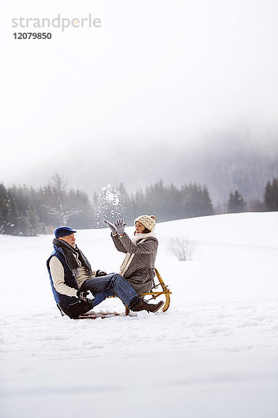 Seniorenpaar mit Rodelspaß in verschneiter Landschaft