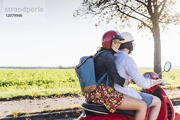 Fröhliches junges Paar auf dem Motorroller mit Rucksack auf dem Rücken