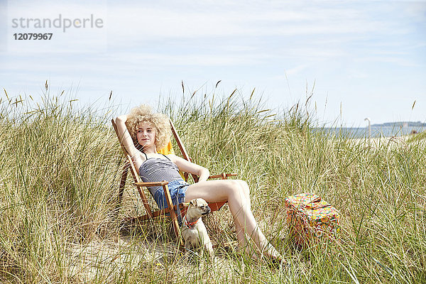 Porträt einer jungen Frau  die auf einem Strandkorb in den Dünen sitzt und etwas beobachtet.