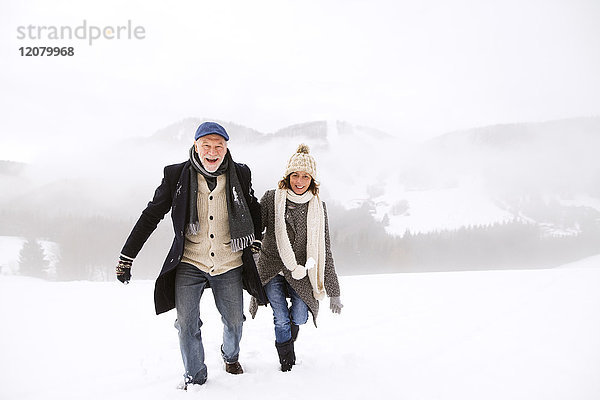 Porträt eines glücklichen Seniorenpaares beim Wandern in verschneiter Landschaft