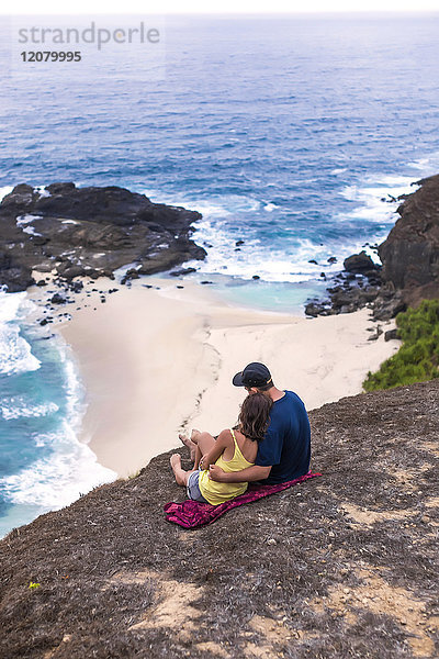 Indonesien  Lombok  Paar an der Küste sitzend mit Blick auf das Meer