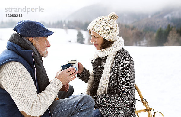 Seniorenpaar bei einer Pause mit heißen Getränken in verschneiter Winterlandschaft