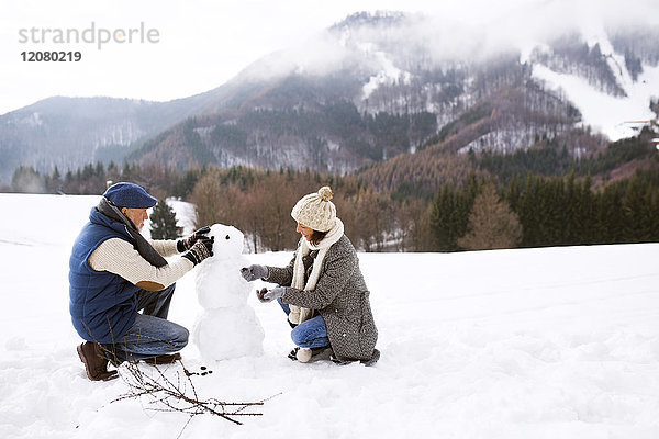 Seniorenpaar baut Schneemann in Winterlandschaft auf