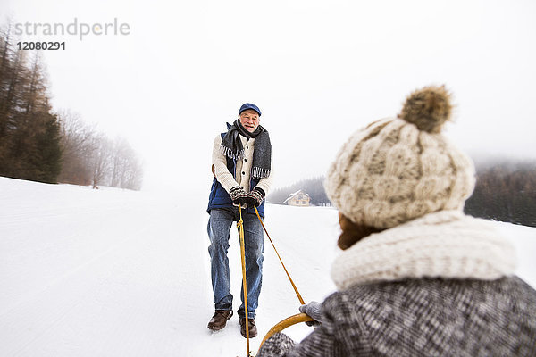 Glückliches Seniorenpaar beim Schlittenfahren in verschneiter Landschaft