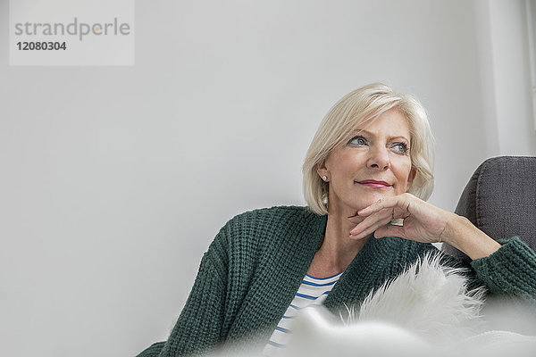 Porträt der lächelnden Seniorin auf der Couch im Wohnzimmer