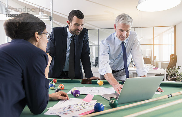 Geschäftsleute stehen mit Laptop am Billardtisch und diskutieren die Anlagestrategie.