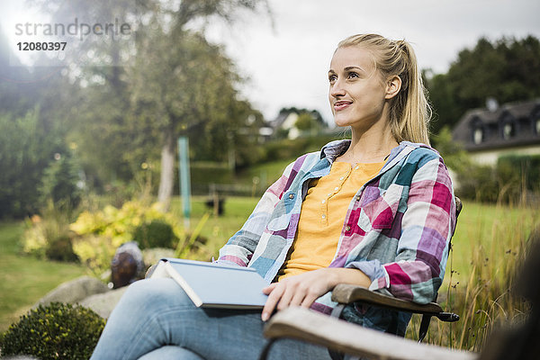 Lächelnde junge Frau mit Buch Entspannung im Garten