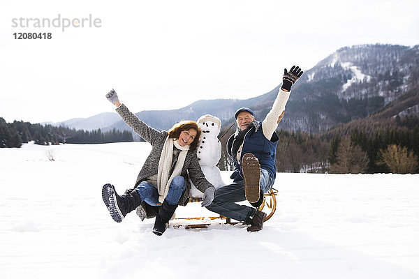 Seniorenpaar posiert mit Schneemann auf Schlitten in Winterlandschaft