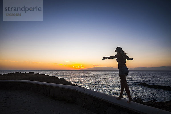 Spanien  Teneriffa  Frau  die bei Sonnenuntergang an der Wand balanciert.