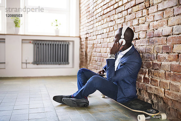 Geschäftsmann sitzt auf dem Longboard und hört Musik mit Kopfhörern.