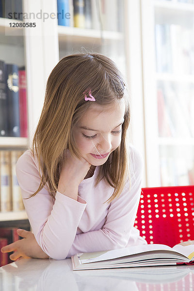 Porträt eines lächelnden kleinen Mädchens am Tisch beim Lesen eines Buches
