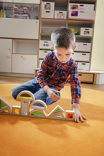 Junge  der im Kindergarten Holzspielzeugformen auf dem Teppich auskleidet