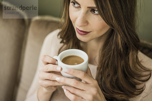 Porträt einer Frau  die auf der Couch sitzt und eine Tasse weißen Kaffee trinkt.