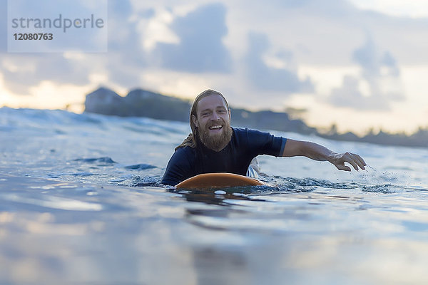 Porträt eines glücklichen Mannes auf dem Surfbrett auf dem Meer liegend