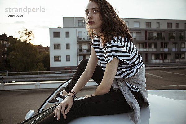 Seriöse junge Frau auf dem Autodach sitzend