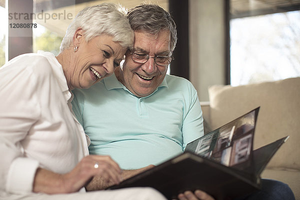 Fröhliches Seniorenpaar auf der Couch beim Betrachten des Fotoalbums